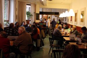 Gäste an gedeckten Tischen im Gastraum des Cafés